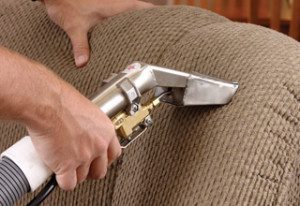 Person cleaning a beige fabric couch with a vacuum tool.