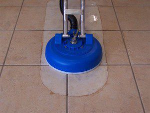 Tile floor being cleaned with a blue rotary scrubber.